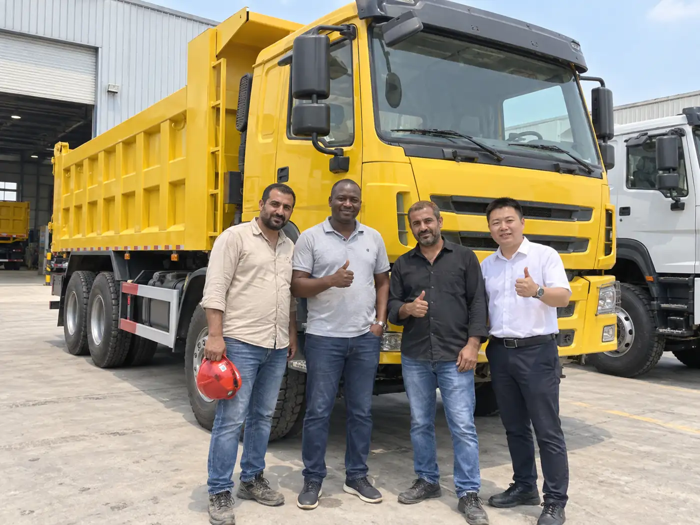 International customers viewing a yellow dump vehicle at the production facility